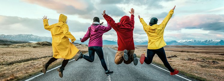 Vier Personen in Regenmänteln springen auf einer Straße.