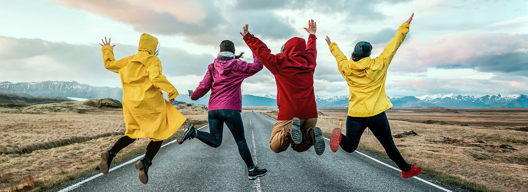 Vier Personen in Regenmänteln springen auf einer Straße.